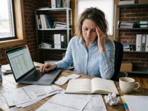 Cheffe d'entreprise fatiguée devant des factures et un tableur, illustrant la perte de temps liée à la gestion financière des petites entreprises
